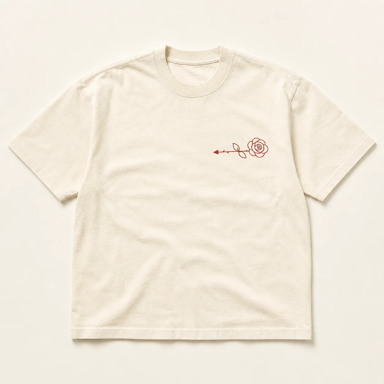 Cream heavyweight tee laid flat, small dark red rose with a left-pointing arrow stem printed on the left chest